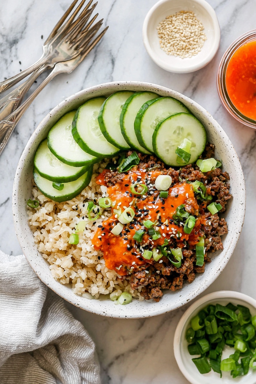 Korean Beef Bowl Recipe 6 A white speckled bowl contains three main layers arranged side by side: on the left, a bed of light brown rice with a soft, grainy texture; in the middle, a layer of cooked ground meat mixed with small pieces of translucent cooked onion, all topped with a drizzle of bright orange-red sauce, sprinkled with black and white sesame seeds, and garnished with small slices of fresh green scallions; on the right, five overlapping slices of fresh cucumber with pale green flesh and dark green skin. The bowl sits on a white marbled surface with a light grey cloth napkin and two silver forks beside it. Around the bowl are small white dishes, one with light sesame seeds and another with chopped green scallions, and a small glass container with orange-red sauce. photo taken with an iphone --ar 2:3 --v 7 - Korean Beef Bowl, Korean Beef Bowl recipe, easy Korean beef bowl, quick beef bowl dinner, flavorful Korean beef bowl