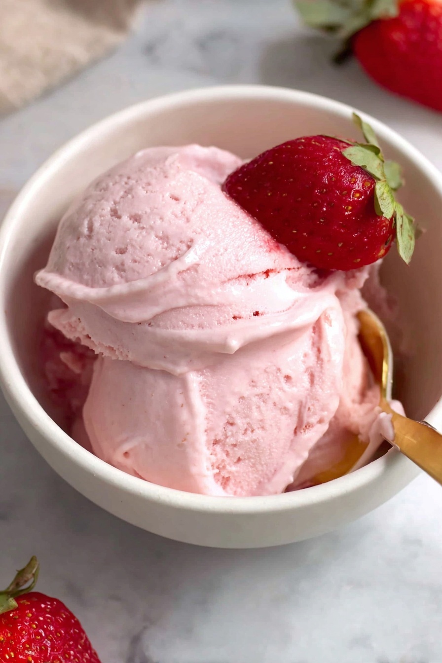 Strawberry Cottage Cheese Ice Cream Recipe 6 A white bowl filled with smooth, creamy pink strawberry ice cream with a soft texture, softly swirled on top with gentle curves. A single half strawberry with bright red and green leaves rests on the ice cream’s surface near the top edge. A gold spoon gently scoops into the ice cream at the front right side of the bowl. The bowl sits on a white marbled surface with parts of a whole strawberry in the background. Photo taken with an iphone --ar 2:3 --v 7 - Strawberry Cottage Cheese Ice Cream, healthy berry ice cream, easy summer dessert, low-fat ice cream recipes, protein-rich frozen treat