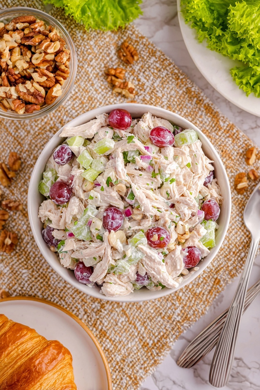 Chicken and Grape Salad Recipe 8 A white bowl filled with a creamy chicken salad layered with thick white shredded chicken pieces, scattered purple-red grape halves, small light green celery slices, and tiny bits of red onion, all mixed with a white creamy dressing with specks of green herbs. The bowl sits on a textured beige woven cloth, surrounded by a glass bowl of chopped light brown nuts, a golden brown croissant on a white plate, two silver spoons, and some bright green lettuce leaves on a white marbled surface. Photo taken with an iphone --ar 2:3 --v 7 - Chicken and Grape Salad, Chicken and Grape Salad Ingredients, Easy Chicken and Grape Salad, Healthy Chicken Grape Salad, Quick Chicken Salad with Grapes